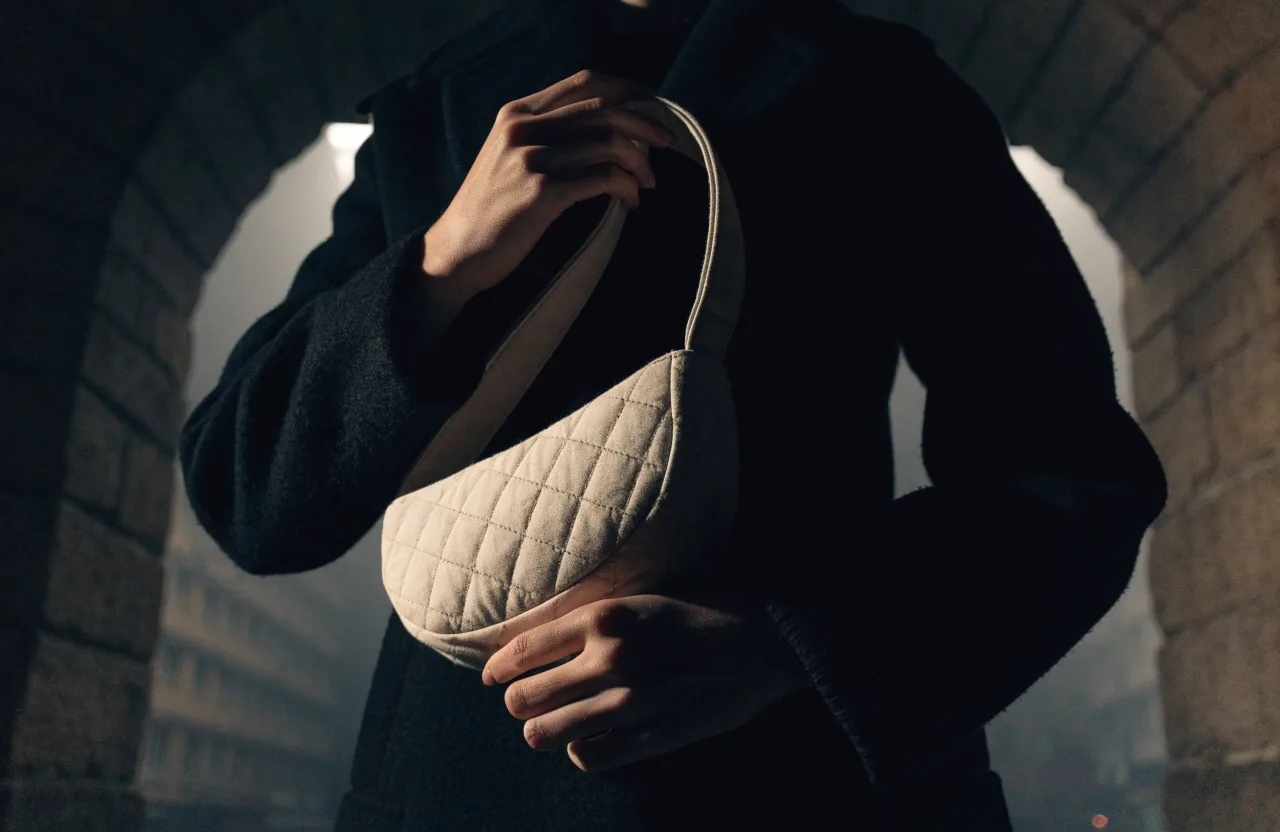 A soft crescent bag on a wet stone ledge against a dark brick wall under a hard left key light at night