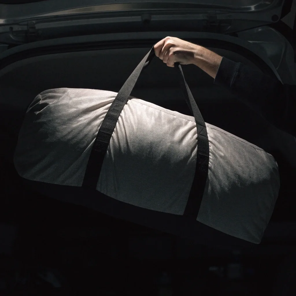 A duffel bag lifted by its handle from a car trunk under a single lamp at night