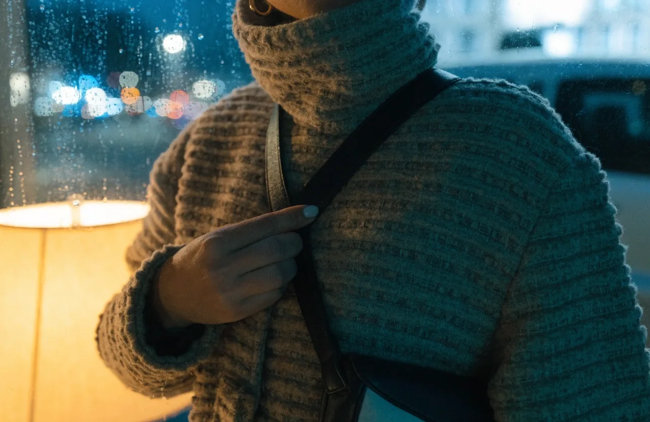 A crossbody bag hanging from a fogged metal railing with city night lights far behind