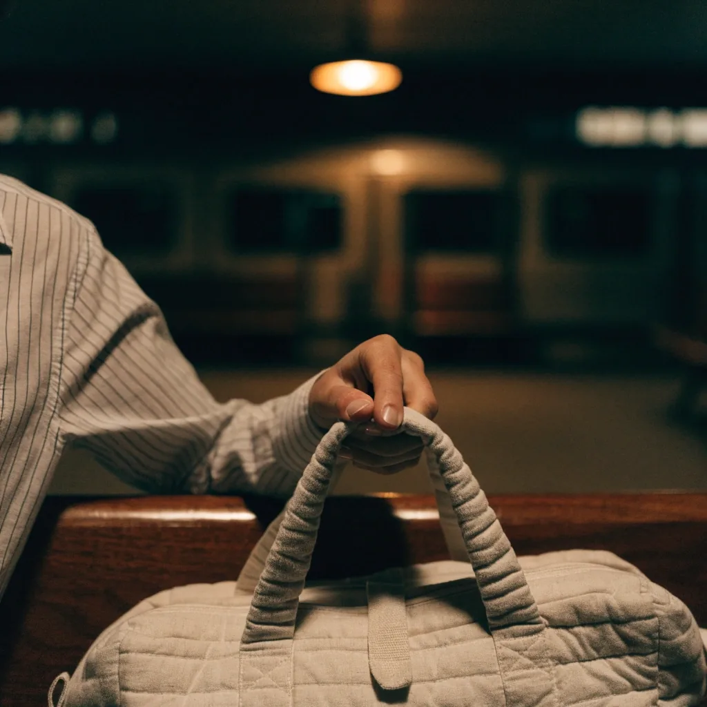 A hand lifting a soft quilted cotton purse by its top handle from dark wet pavement at night
