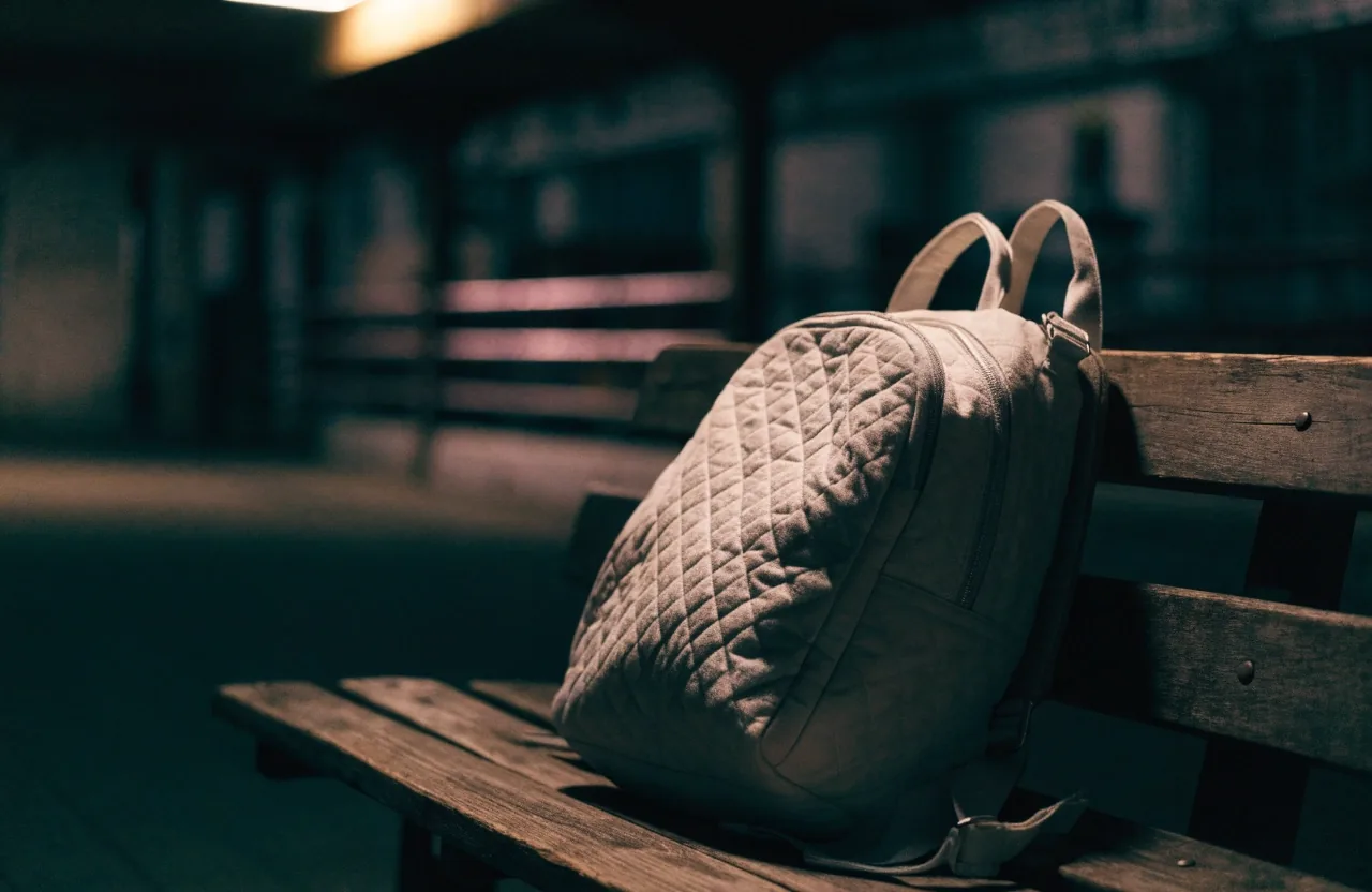 A canvas weekender bag on fog-wet pier boards at night under a single work lamp